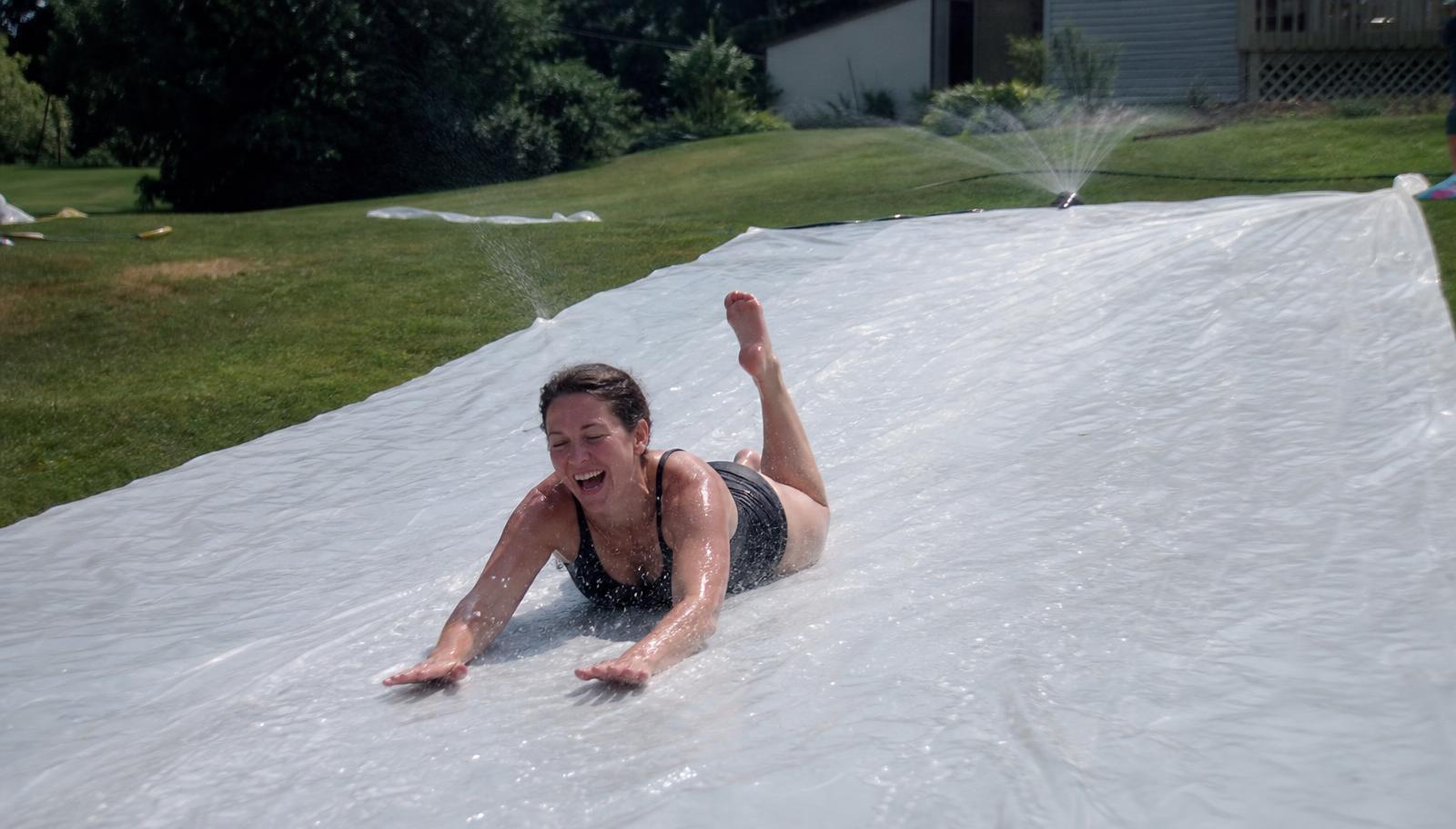100 Ft Slip and Slide: an adult sliding down a soaked, 10 ft wide run of plain white plastic slip and slide sheeting